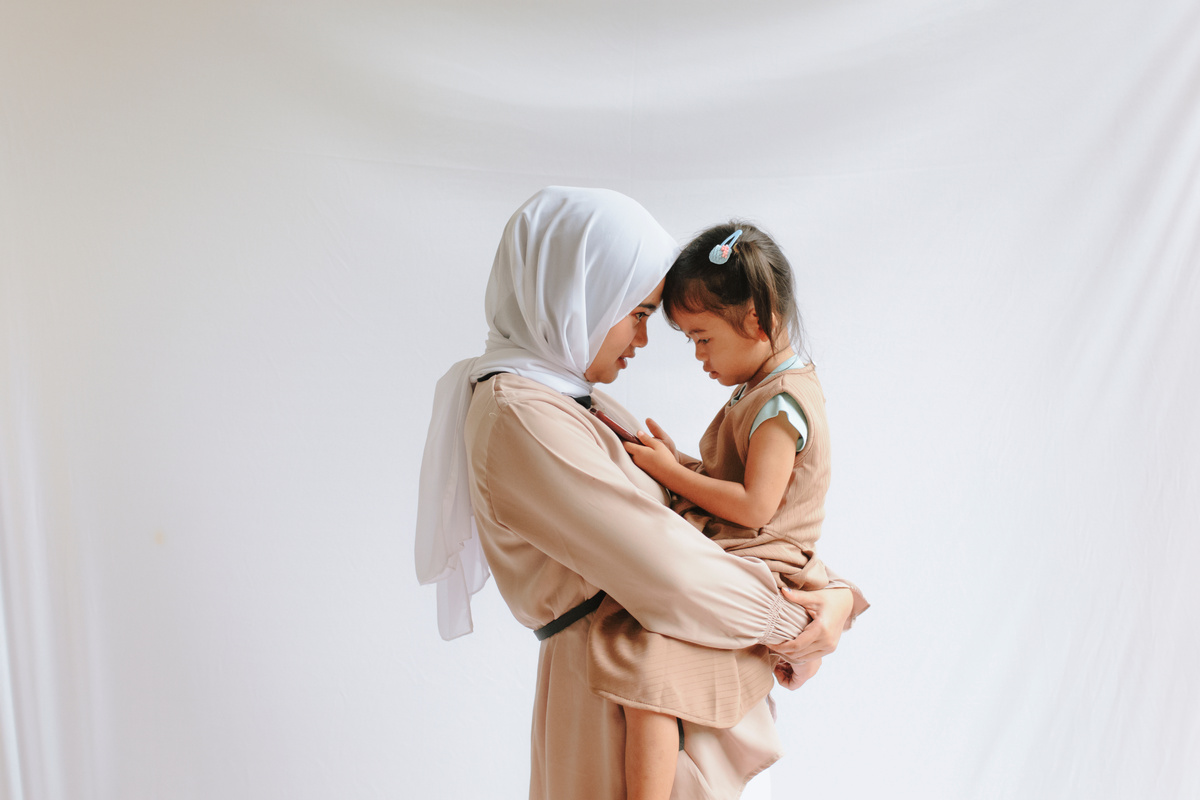 Mother in Hijab Carrying Her Daughter in Brown Dress